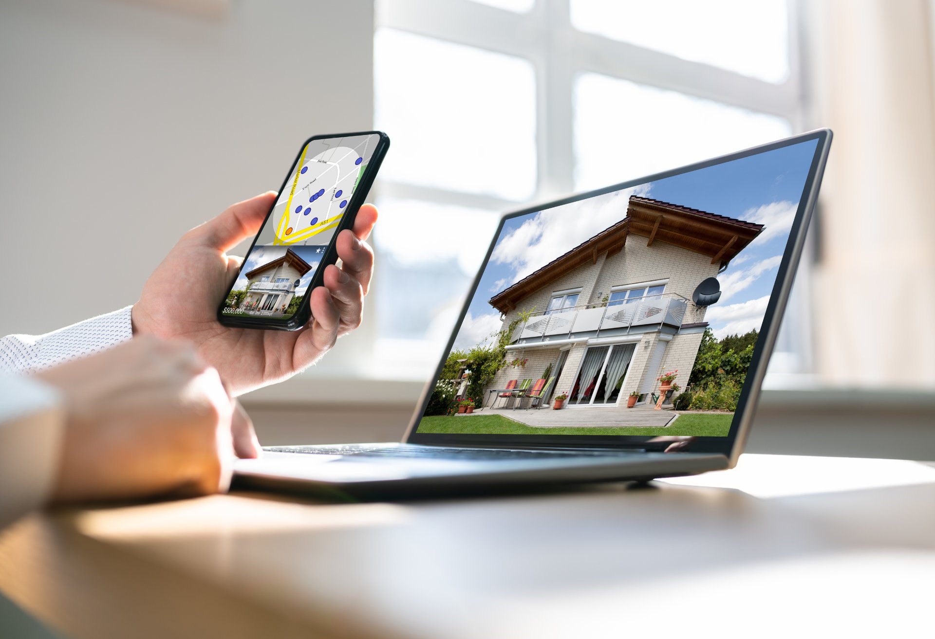 Person using smartphone and laptop to view property listings online